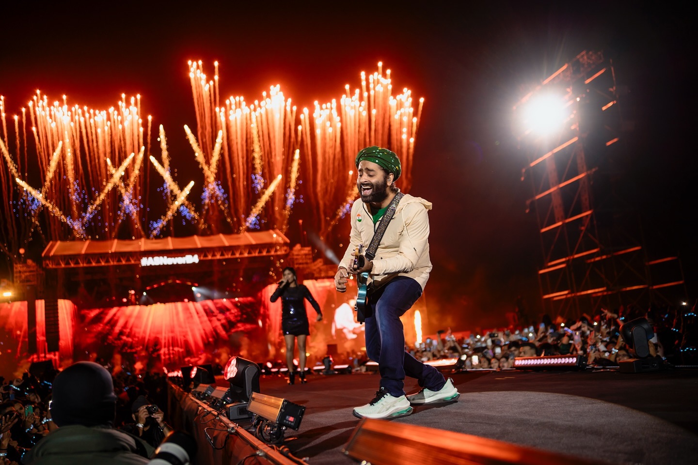 Arijit Singh performing live on stage in front of a large crowd with fireworks in the background