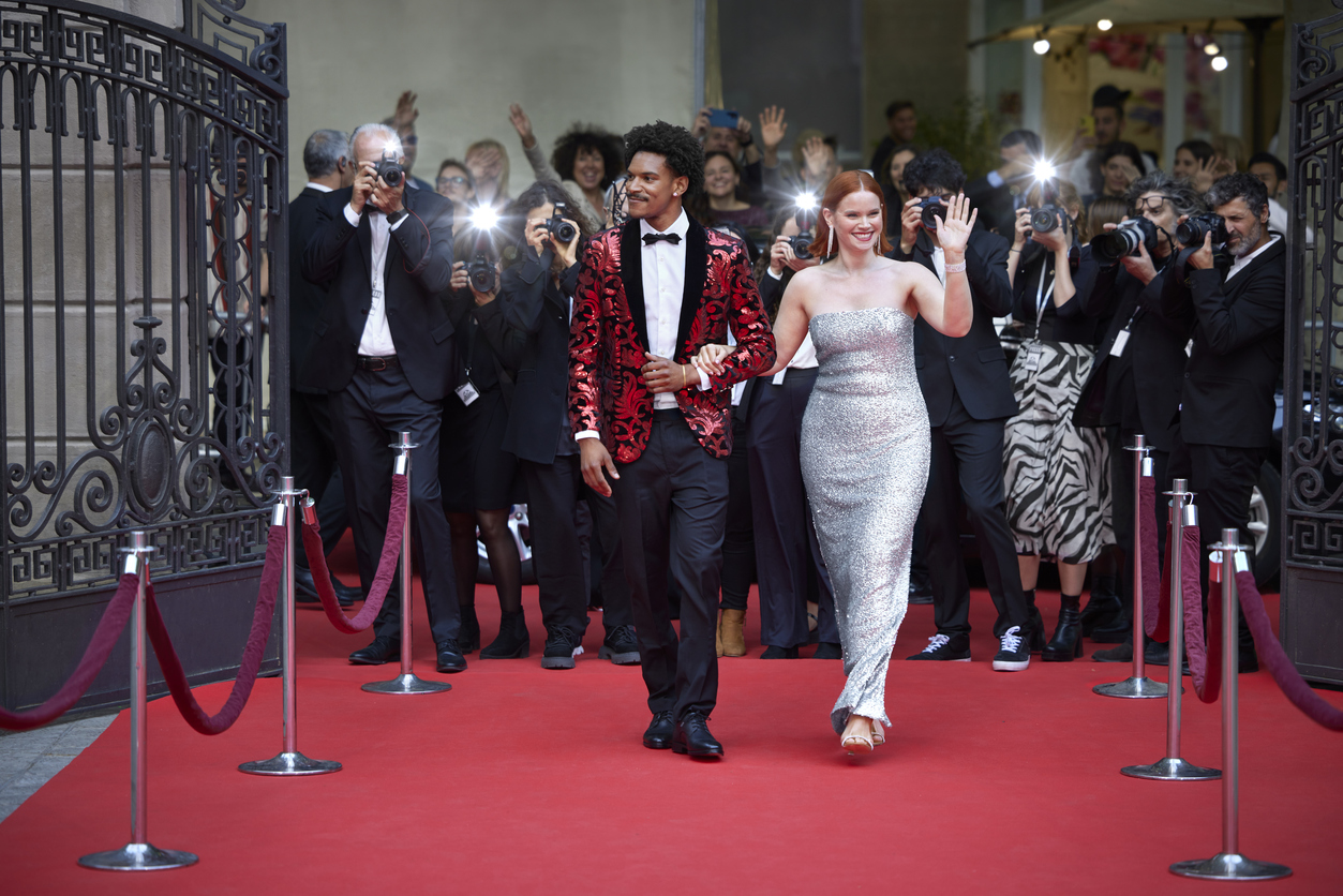 Celebrities walk the red carpet while photographers take pictures at a public event