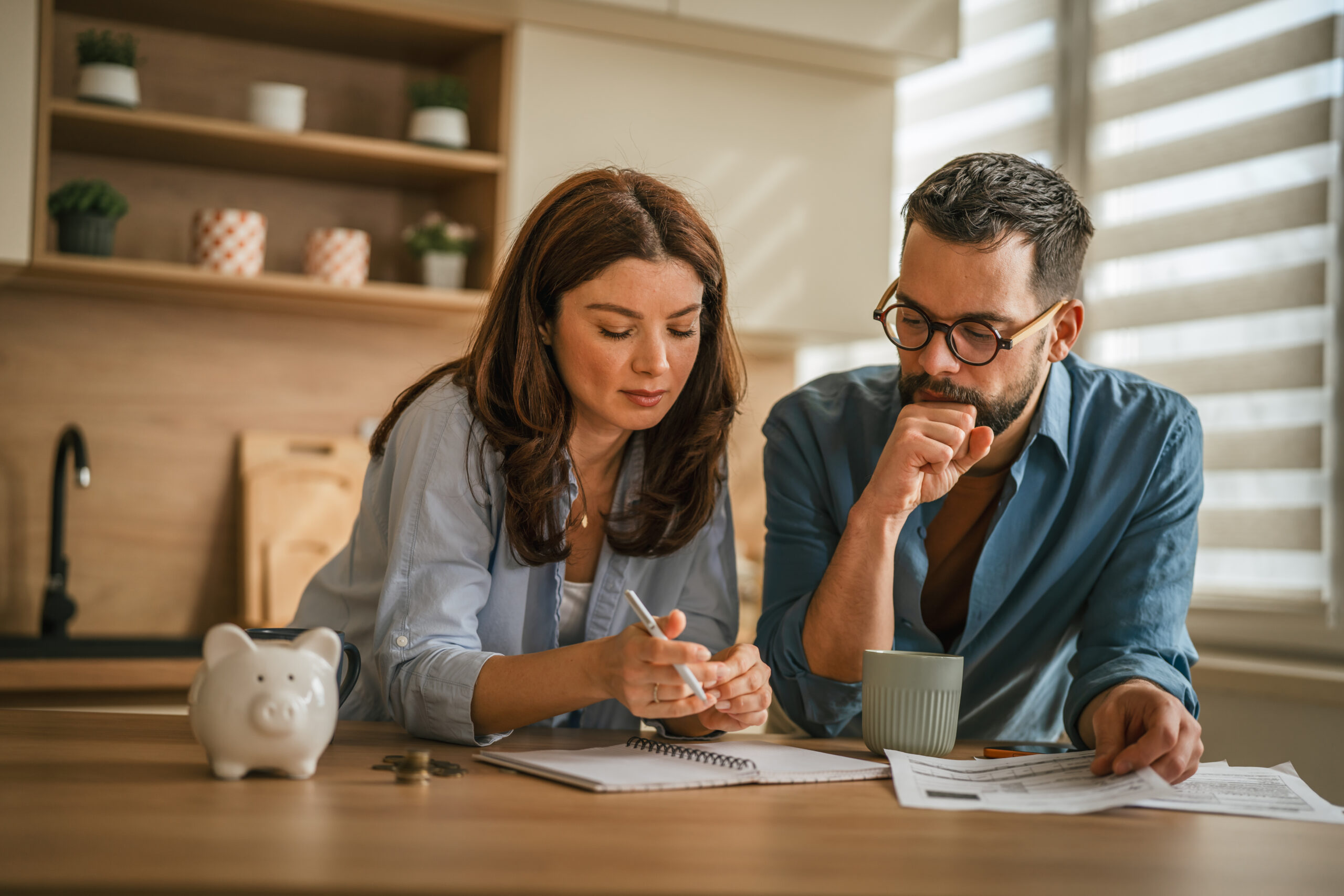 Couple discussing finances and reviewing bills at home while planning shared expenses and a joint bank account.