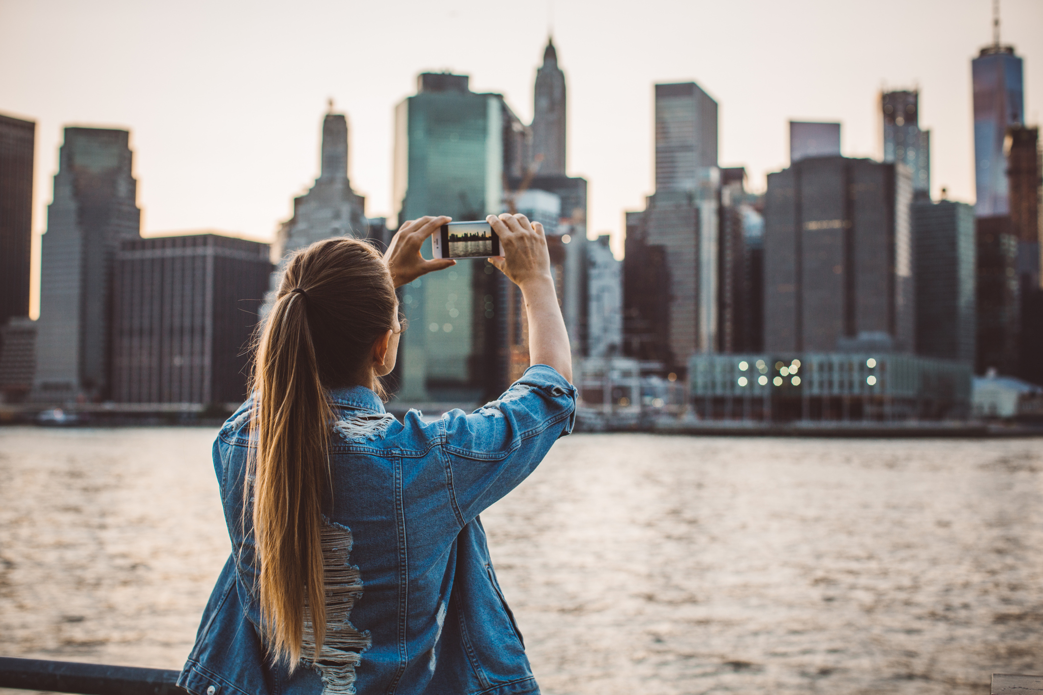 Woman taking a photo of a city skyline, representing travel goals and saving money for travel planning.